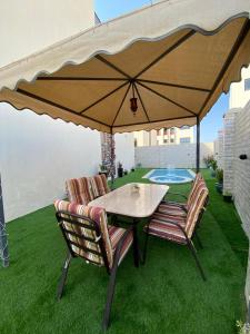 ein Tisch und Stühle unter einem großen Regenschirm auf einem Rasen in der Unterkunft ALZumorod Luxury Villa in Ma‘ābīlah