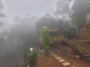 a house in the fog with a tree in front of it at Mistvalley Hut in Chithragiri