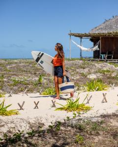 una mujer parada en la playa sosteniendo una tabla de surf en Rancho Do Peixe, en Prea