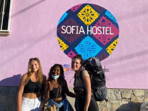 three women standing in front of a pink wall at Sofia Hostel Cabo in Cabo San Lucas
