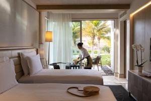 Jumeirah Muscat Bay في مسقط: رجل واقف في غرفة الفندق سريرين