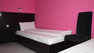 a bed with a chair in a room with a pink wall at Motel Park Rogatica in Rogatica