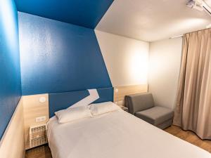 a bedroom with a blue wall and a bed and a chair at ibis Budget Millau Viaduc in Millau