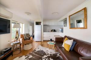 a living room with a brown leather couch and a kitchen at Y Vue - Beachside Apartment with Ocean Views in Wye River