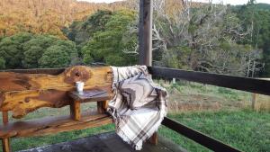 彭古因Rustic Hut Bush Retreat的木凳坐在门廊上,边喝咖啡