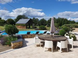 patio con tavolo e ombrellone accanto alla piscina di Maison de Campagne de charme avec piscine privée classée 3 étoiles a Champigné