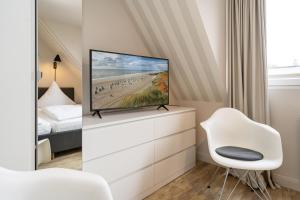 ein Schlafzimmer mit einem TV auf einer Kommode mit einem weißen Stuhl in der Unterkunft Süderliebe in Westerland