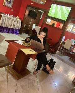 Hotel Astoria في دوالا: امرأة تجلس على طاولة مع جهاز كمبيوتر محمول