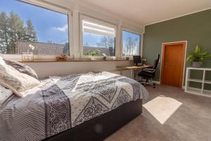 een slaapkamer met een bed, een bureau en ramen bij Ferienwohnung Kathis Eifelblick in Simmerath