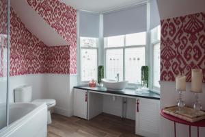 Un baño con papel pintado rojo y blanco y una bañera y un lavabo. en One Sandringham - Boutique Seaside Home in Ilfracombe, en Ilfracombe 9 fotos más