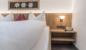 Una cama con almohadas blancas y un teléfono en una mesa. en Pension Edelweiss, en Sölden