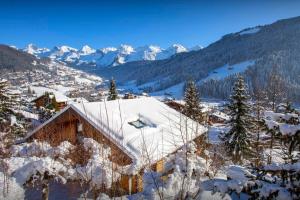 a house covered in snow with mountains in the background at Chalet Musini - OVO Network in Le Grand-Bornand