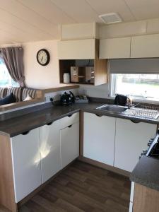 a kitchen with white cabinets and a clock on the wall at Flosh Caravan, Manor House Park in Mawbray