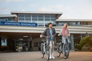 two people riding bikes in front of a building at WestCord ApartHotel Boschrijck in West-Terschelling
