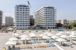 a beach with white umbrellas and chairs and buildings at Luxury Sahara Noir Mamaia Nord in Mamaia