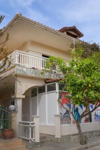 een wit huis met een balkon en een boom bij SAND rooms to let in Nea Roda