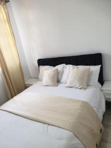Cama blanca con almohadas blancas y cabecero negro en Lovely 2 and 1 bedroom guest units Karen, en Nairobi