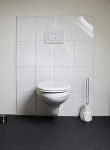 een badkamer met een toilet in een witte betegelde muur bij De Duun in Nes
