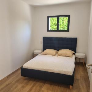 a bedroom with a bed with a blue headboard and two windows at Rez de villa avec piscine, wifi, jardin clôturé in Penta-di-Casinca