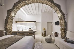 a bedroom with an archway with a bed and a desk at Elaia Luxury Suites Mykonos in Mikonos