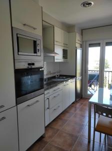 een keuken met witte kasten, een tafel en een magnetron bij Piso en primera linea de Playa en Laxe in Laxe