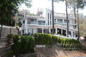 a white house on a hill with trees at The Golden Sunrise Hotel in Nainital