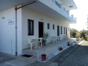a white house with white chairs and a porch at Villa Kaloudis Rooms in Agios Georgios