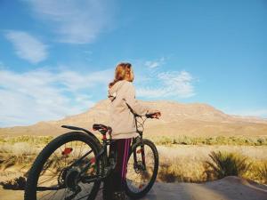 Una mujer parada junto a una bicicleta en el desierto en Dar Hnini, en Zagora