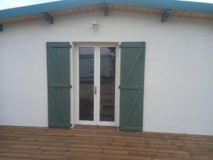 a white house with green doors on a patio at Une petite maison et sa prairie in Villefargeau