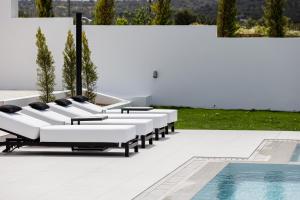 a row of white lounge chairs next to a pool at Alma Villa, 2000m2 Luxury Living, by ThinkVilla in Angeliana