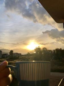 une personne tenant une tasse de café au coucher du soleil en arrière-plan dans l'établissement Apartman Playa, à Igalo