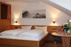 a bedroom with a bed with white pillows and a table at Gasthof und Pension Neuwirt in Lenggries