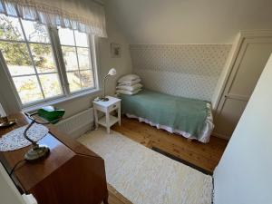 um pequeno quarto com uma cama, uma mesa e janelas em Tutviksvägen 35 em Vendelsö