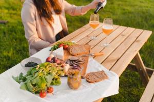 een picknicktafel met een bord eten en twee glazen wijn bij Parcel Tiny House I Les Jardins de la Thillaye in Reux