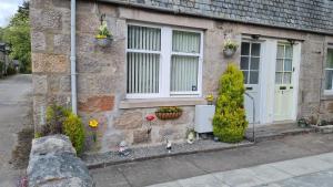 a stone house with a door and flowers in front of it at Deeside Holiday Cottages in Dinnet