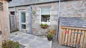 ein Steinhaus mit einem Holzzaun und einem Fenster in der Unterkunft deesideholidaycottages in Dinnet