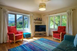 a living room with two red chairs and a flat screen tv at Cherry How - Patterdale - Dog-friendly in Patterdale