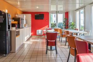 a restaurant with tables and chairs and a red wall at Premiere Classe Rouen Nord - Barentin in Barentin