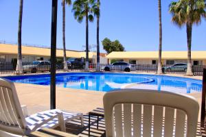 a swimming pool with two lawn chairs and palm trees at HOTEL POSADA DEL DESIERTO in Heroica Caborca