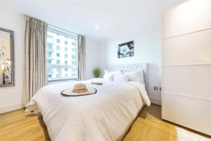 a white bedroom with a bed with a hat on it at Panoramic Riverside Facing - 2 Bed - 2 Bath - 2 Balconies - London Nine Elms in London