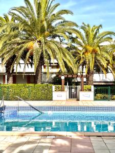 a swimming pool with palm trees in front of a building at L'Escapade Bohème in La Grande-Motte