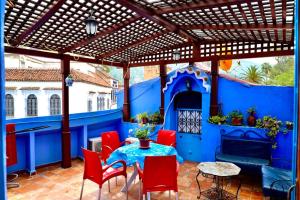 een blauwe patio met een tafel en rode stoelen bij Dar el Khzana in Chefchaouene