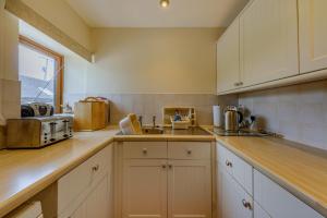 una cucina con armadi bianchi e lavandino di Wren Cottage a Leek