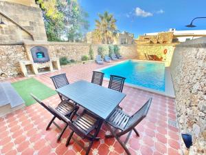 un patio con mesa y sillas junto a una piscina en Villa Rossa Gozo - 5 bedroom ensuite with pool & jacuzzi, en Xewkija