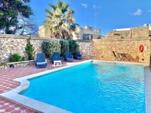 een zwembad met blauwe stoelen en een stenen muur bij Villa Rossa Gozo - 5 bedroom ensuite with pool & jacuzzi in Xewkija