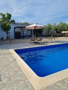 a blue swimming pool with an umbrella and chairs at Lo raconet in L'Ampolla