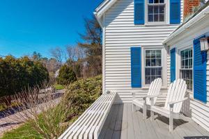 2 chaises blanches assises sur une terrasse couverte d'une maison dans l'établissement Blue Shutters Cottage, à Boothbay Harbor