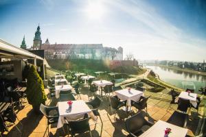a row of tables and chairs on a patio with a river at Hotel Pod Wawelem in Krakow
