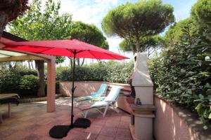 un paraguas rojo y 2 sillas en un patio en Belle villa de Vacances en angle climatisée, domaine TAMARIS, 4 chambres 7-9 couchages, Wifi, accès aux piscines payant, 900m de la mer LRTAMQ10, en Portiragnes