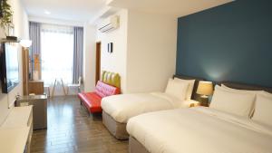 a hotel room with two beds and a red chair at Lukang Holiday Hostel in Lukang